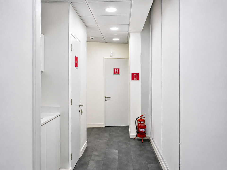 Pasillo de servicio con señalética de baño y extintor en GAES Apoquindo